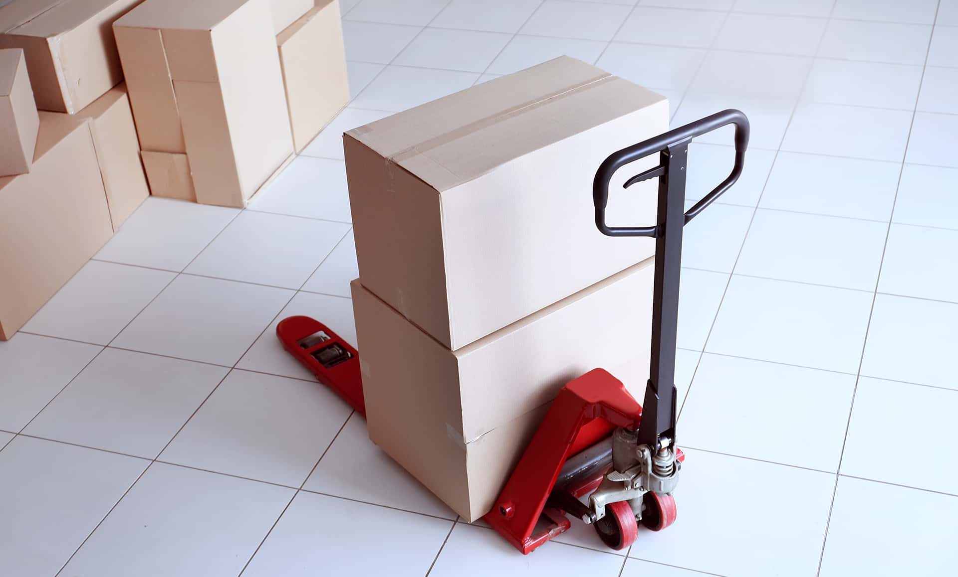 Paletový vozík s dvomi kartónovými škatuľami na bielej dlažbe